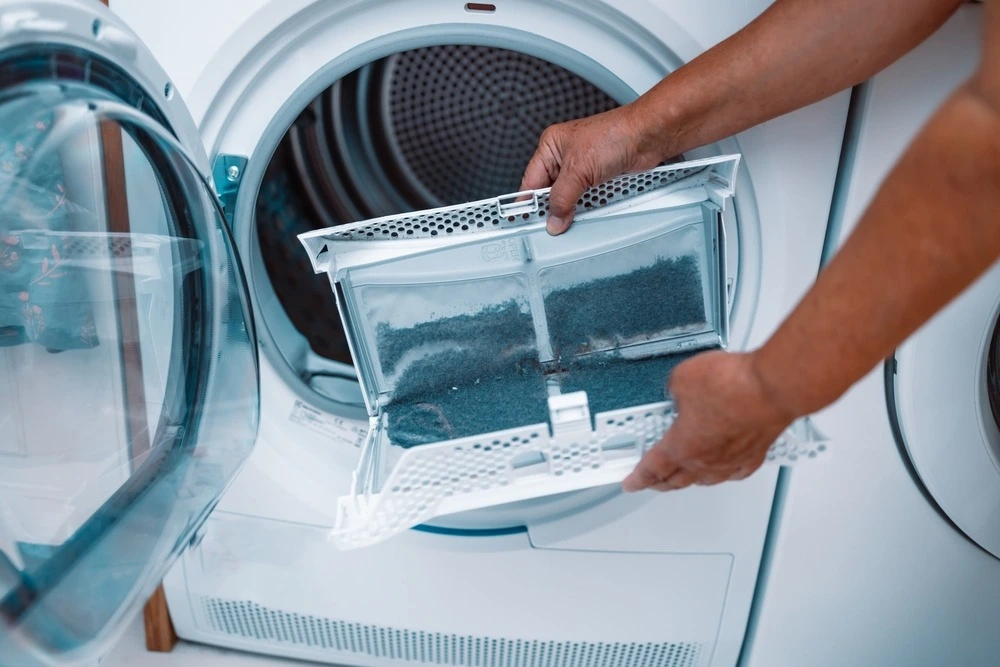 Person cleaning lint screen on commercial dryer